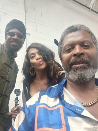 Three people taking a selfie in front of a white brick wall, smiling at the camera