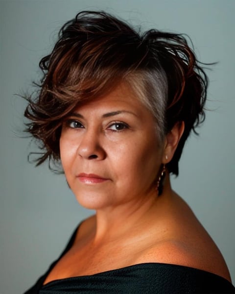 Portrait of a woman with short, layered reddish-brown hair wearing a black off-shoulder top against a gray background